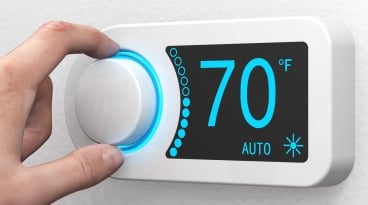 Person's fingers adjusting the knob on a room's wall mounted thermostat.