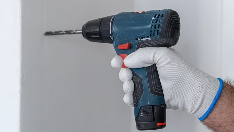 Hand holding a cordless drill against a wall.