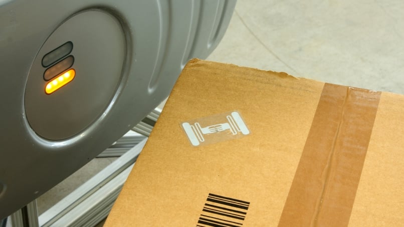 Cardboard package beside an industrial sensor on a conveyor system.
