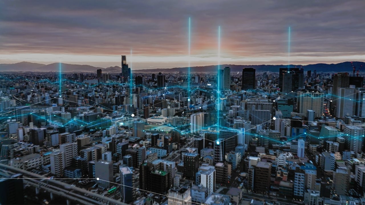 Aerial view of city with connectivity network represented by glowing blue lines and dots.